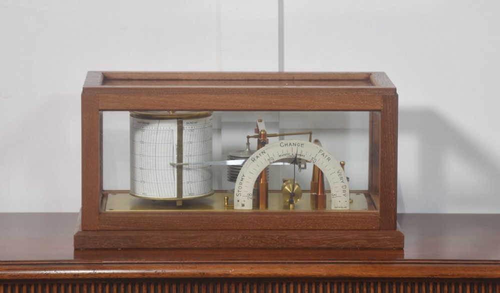 An antique mahogany-cased barograph with glass panels showing a revolving chart drum, brass mechanism, and silvered weather indicator arc.