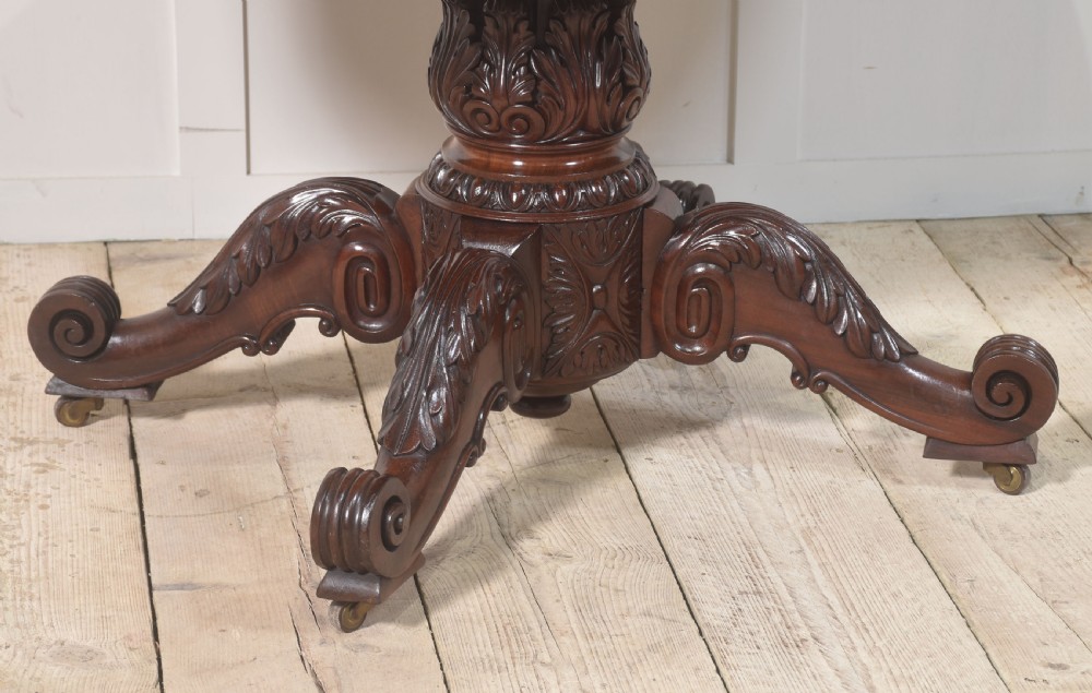 A 19th-century oval mahogany drum table featuring a reeded top edge, frieze drawers, and an elaborately carved acanthus pedestal on scroll legs with brass castors. View II