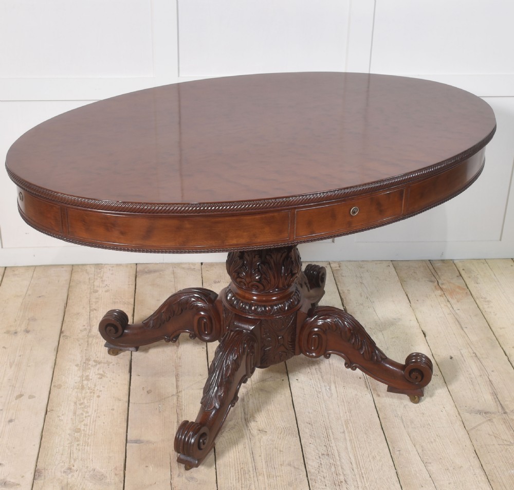A 19th-century oval mahogany drum table featuring a reeded top edge, frieze drawers, and an elaborately carved acanthus pedestal on scroll legs with brass castors. View V
