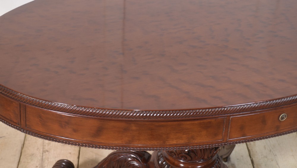 A 19th-century oval mahogany drum table featuring a reeded top edge, frieze drawers, and an elaborately carved acanthus pedestal on scroll legs with brass castors. View VII