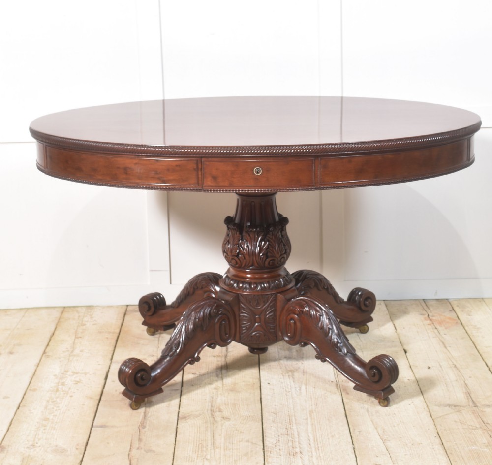 A 19th-century oval mahogany drum table featuring a reeded top edge, frieze drawers, and an elaborately carved acanthus pedestal on scroll legs with brass castors. View VIII