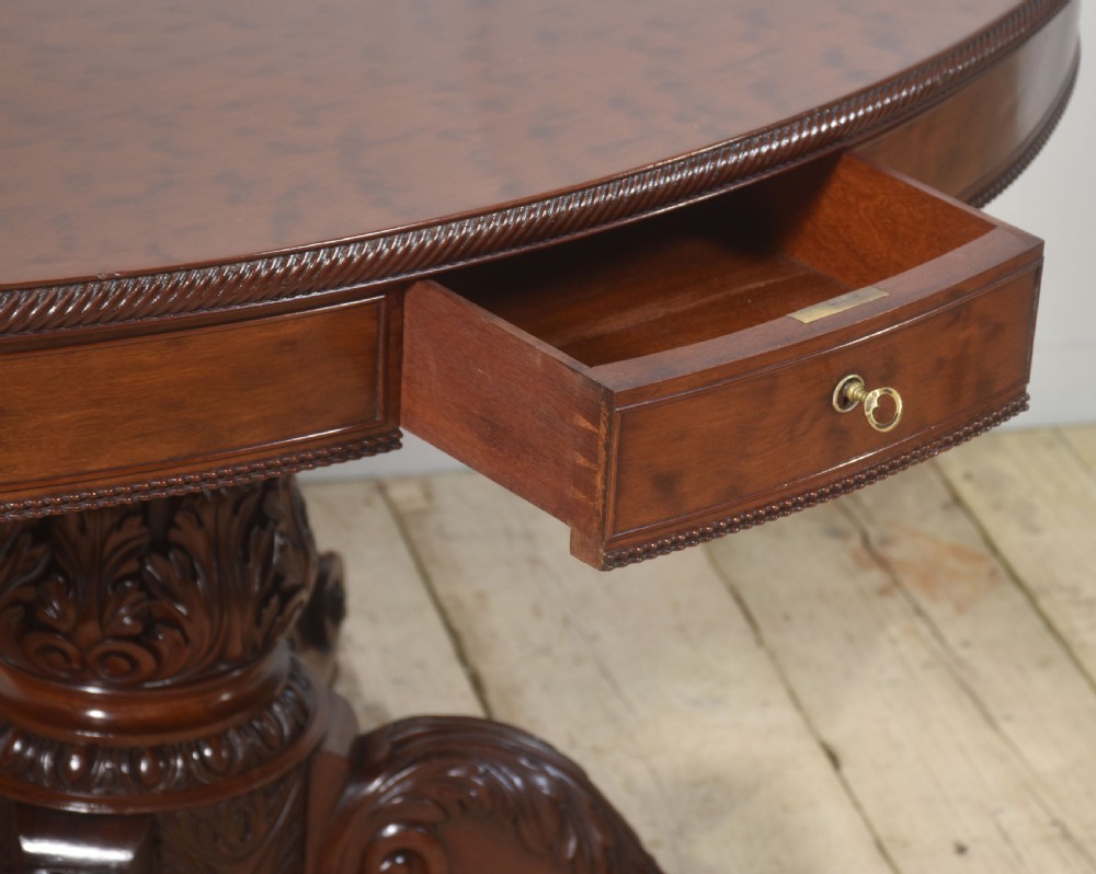 A 19th-century oval mahogany drum table featuring a reeded top edge, frieze drawers, and an elaborately carved acanthus pedestal on scroll legs with brass castors. View XI