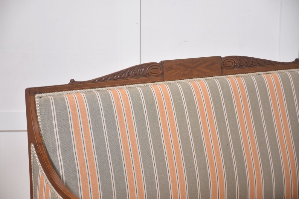 An Edwardian satinwood inlaid two-seater settee with striped orange and grey fabric upholstery, resting on turned front legs with brass castors. View VI