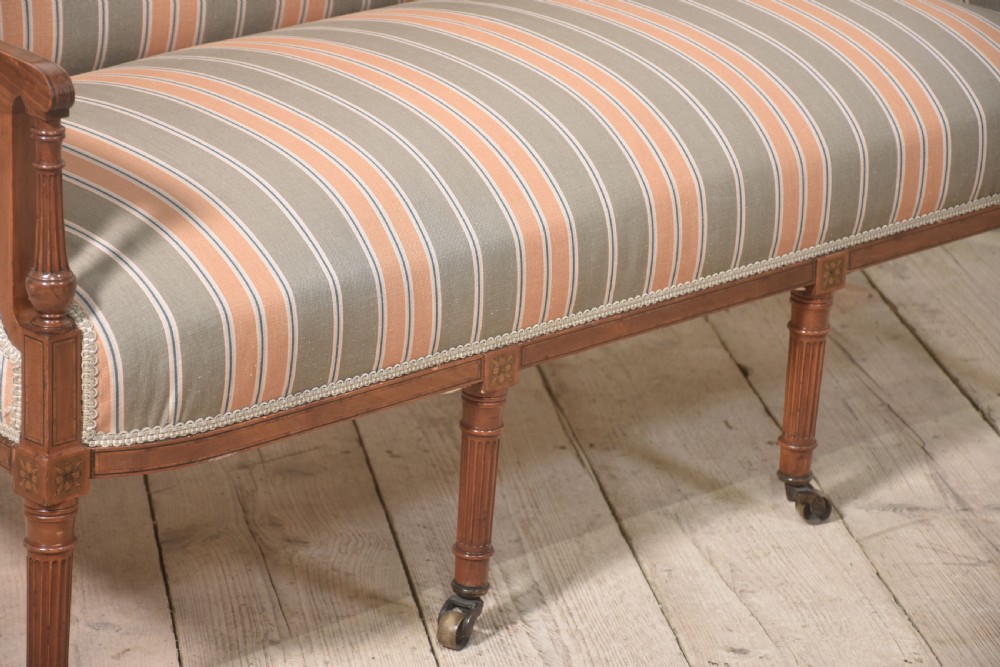 An Edwardian satinwood inlaid two-seater settee with striped orange and grey fabric upholstery, resting on turned front legs with brass castors. View VIII