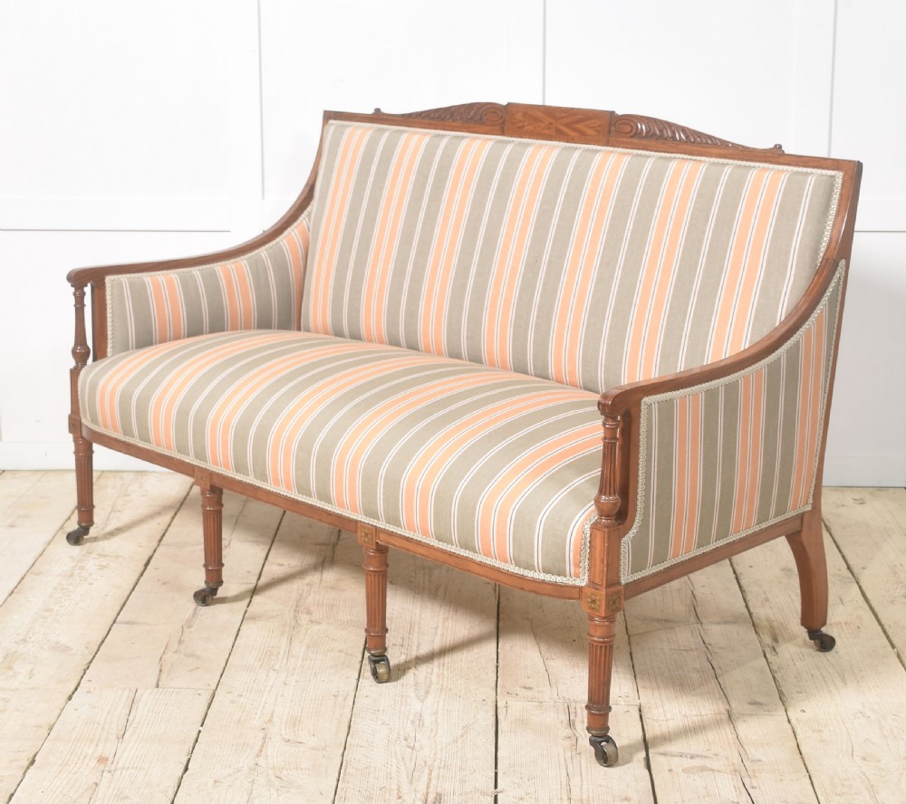 An Edwardian satinwood inlaid two-seater settee with striped orange and grey fabric upholstery, resting on turned front legs with brass castors. View IX