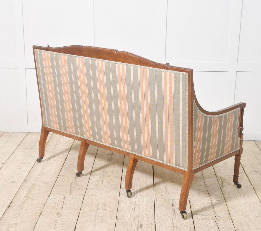 An Edwardian satinwood inlaid two-seater settee with striped orange and grey fabric upholstery, resting on turned front legs with brass castors. View X