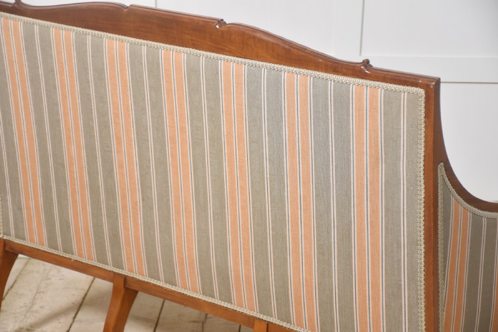 An Edwardian satinwood inlaid two-seater settee with striped orange and grey fabric upholstery, resting on turned front legs with brass castors. View XI