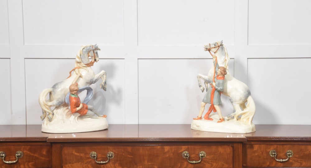 A pair of glazed cream and grey porcelain figures depicting rearing horses held by handlers on naturalistic bases. View VI
