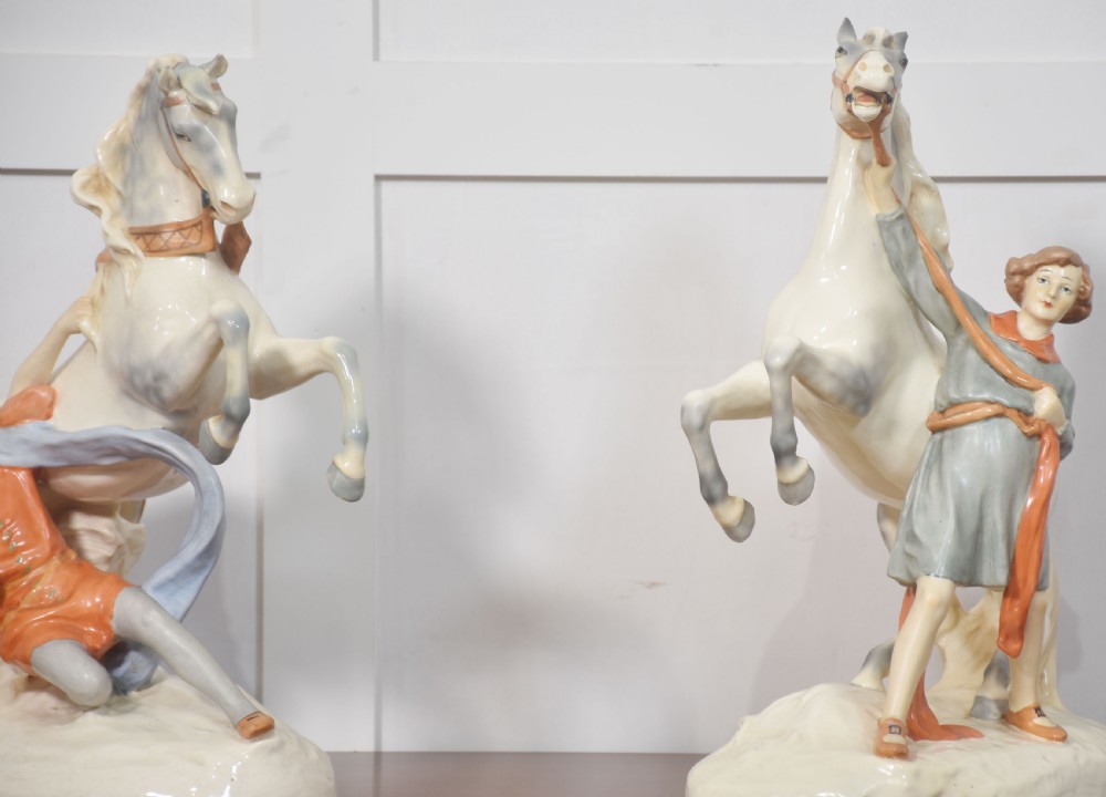 A pair of glazed cream and grey porcelain figures depicting rearing horses held by handlers on naturalistic bases. View VII