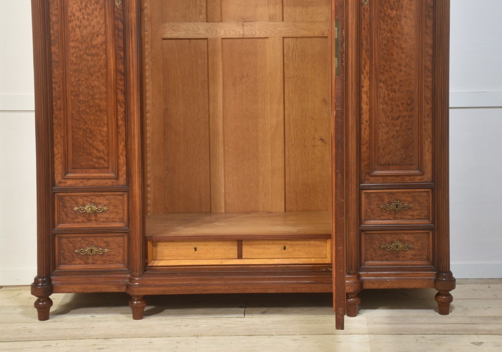 A French Louis XVI style mahogany triple armoire featuring a central mirrored door flanked by carved timber panels and lower drawers. View III