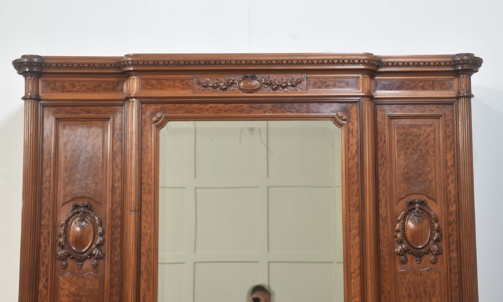 A French Louis XVI style mahogany triple armoire featuring a central mirrored door flanked by carved timber panels and lower drawers. View VIII
