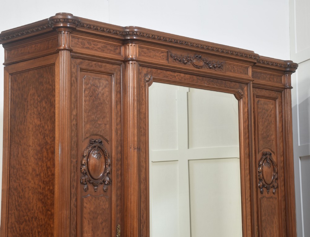 A French Louis XVI style mahogany triple armoire featuring a central mirrored door flanked by carved timber panels and lower drawers. View XII