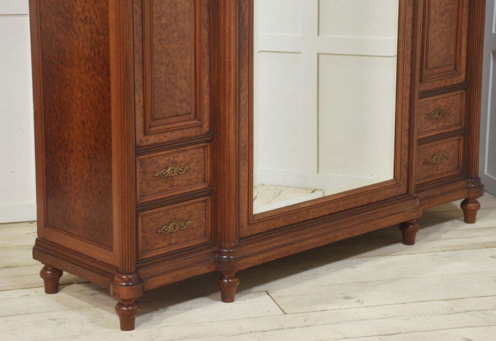 A French Louis XVI style mahogany triple armoire featuring a central mirrored door flanked by carved timber panels and lower drawers. View XIV