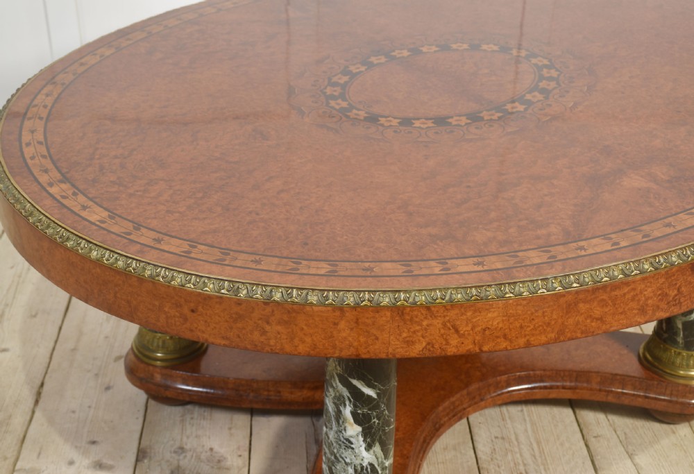 An oval centre table featuring a burr walnut marquetry top, brass rim moulding, four green marble column supports, and a curved stretcher base. View III