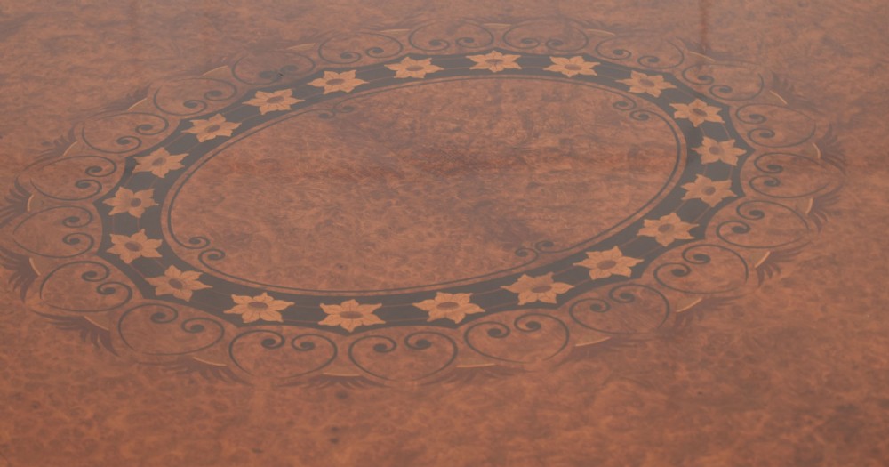 An oval centre table featuring a burr walnut marquetry top, brass rim moulding, four green marble column supports, and a curved stretcher base. View V
