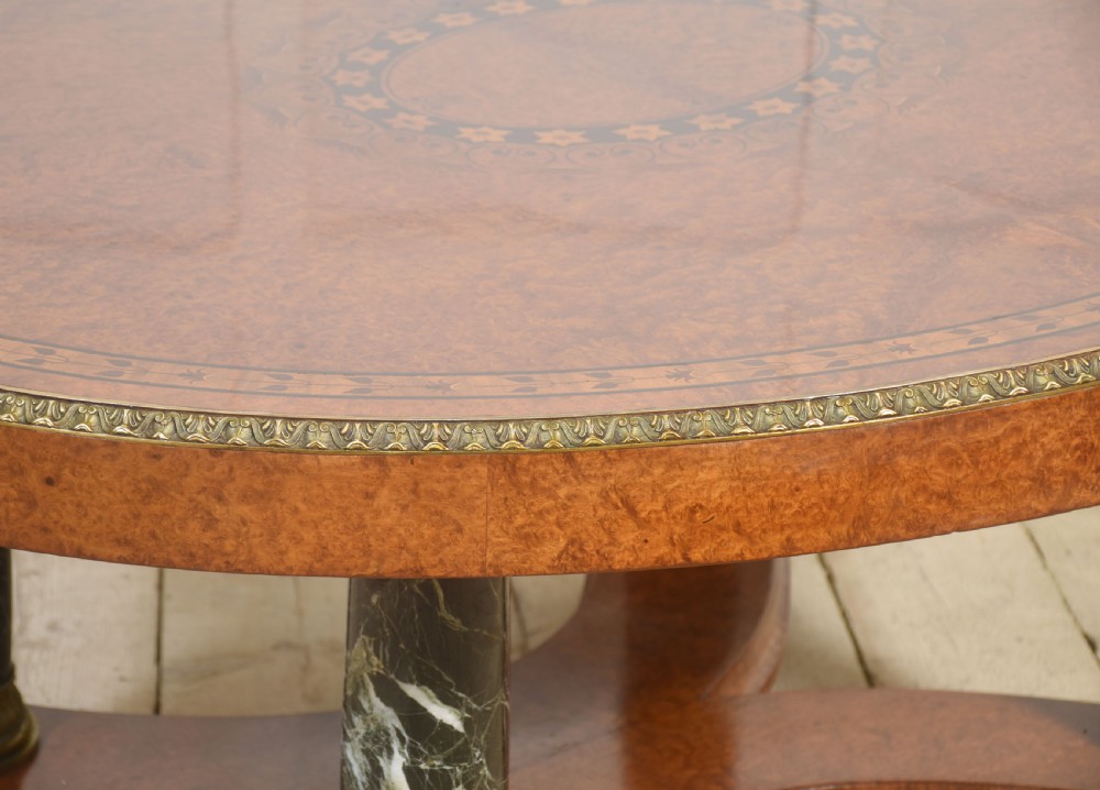 An oval centre table featuring a burr walnut marquetry top, brass rim moulding, four green marble column supports, and a curved stretcher base. View VI