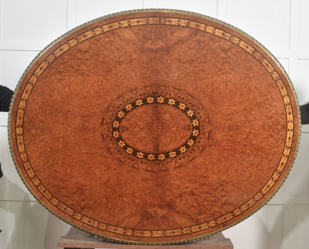An oval centre table featuring a burr walnut marquetry top, brass rim moulding, four green marble column supports, and a curved stretcher base. View IX