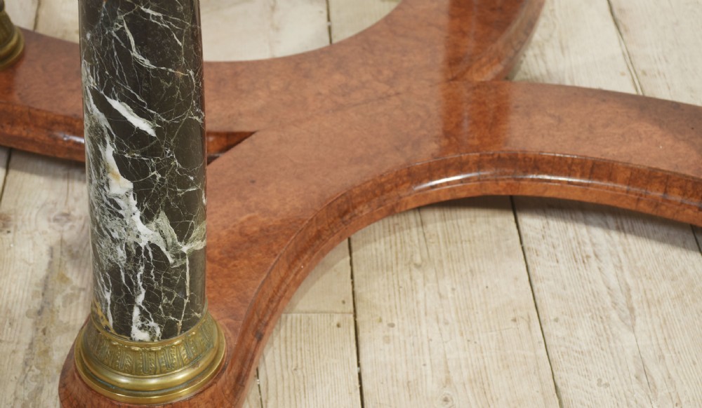 An oval centre table featuring a burr walnut marquetry top, brass rim moulding, four green marble column supports, and a curved stretcher base. View XI