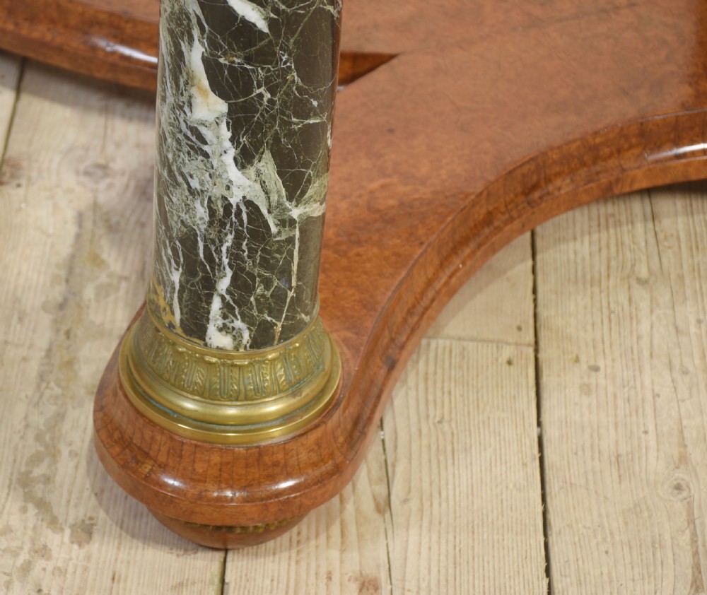 An oval centre table featuring a burr walnut marquetry top, brass rim moulding, four green marble column supports, and a curved stretcher base. View XII