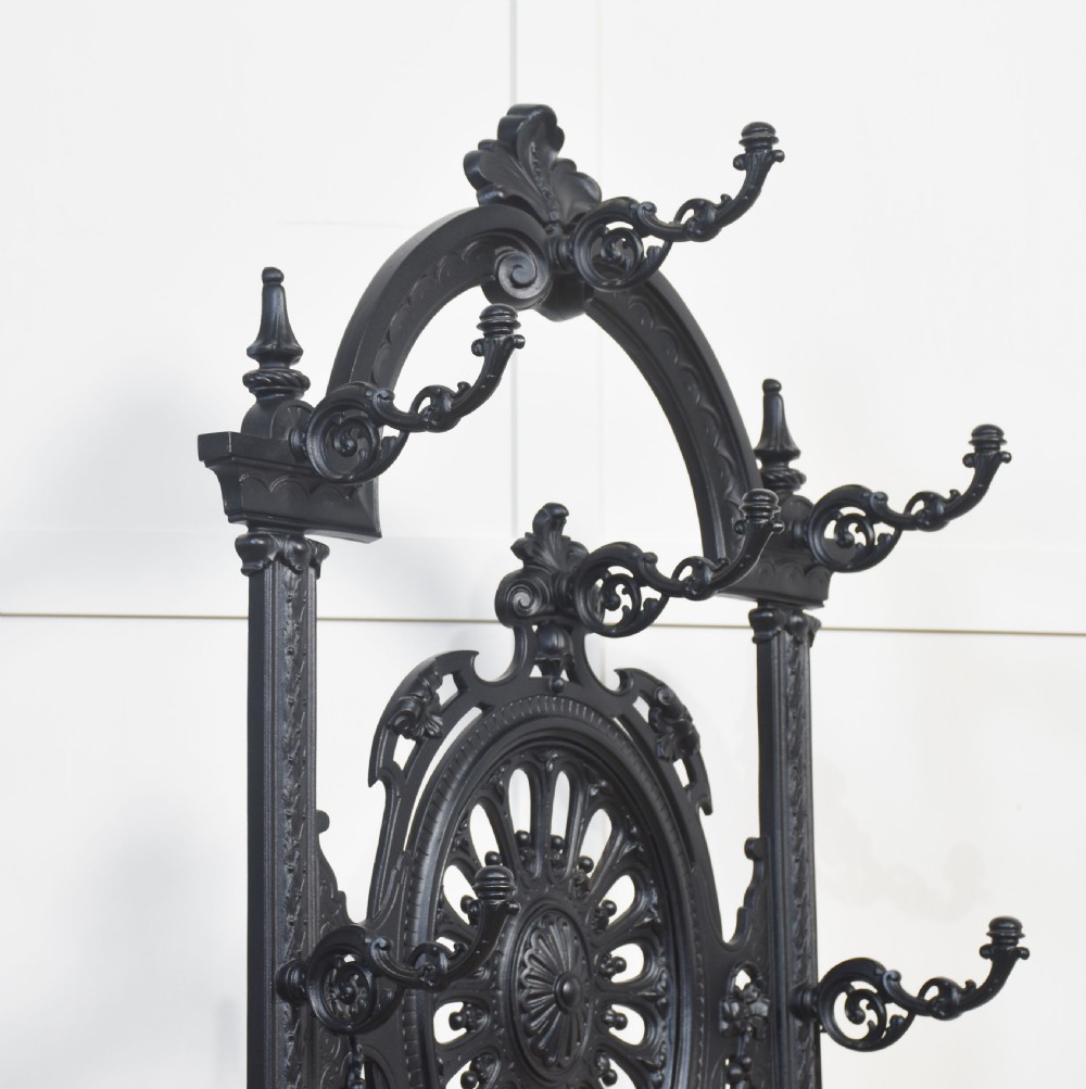 An ornate black cast iron hall stand featuring intricate scrollwork, coat hooks, an umbrella holder, and a fitted drip tray. View XI