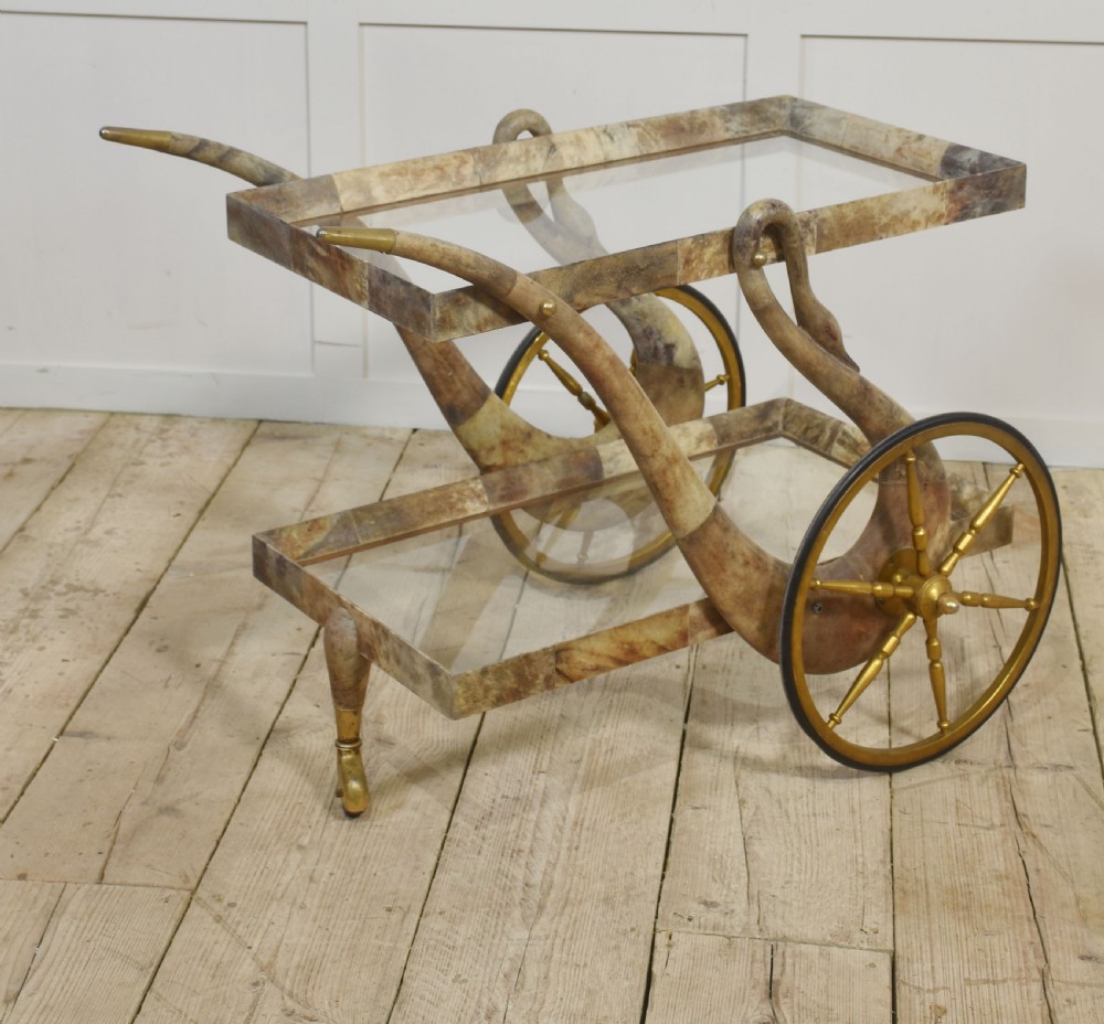 An Italian mid-century drinks trolley crafted with a lacquered goatskin frame, two glass shelves, brass-spoked wheels, and curved handles.