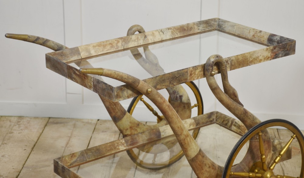 An Italian mid-century drinks trolley crafted with a lacquered goatskin frame, two glass shelves, brass-spoked wheels, and curved handles. View II