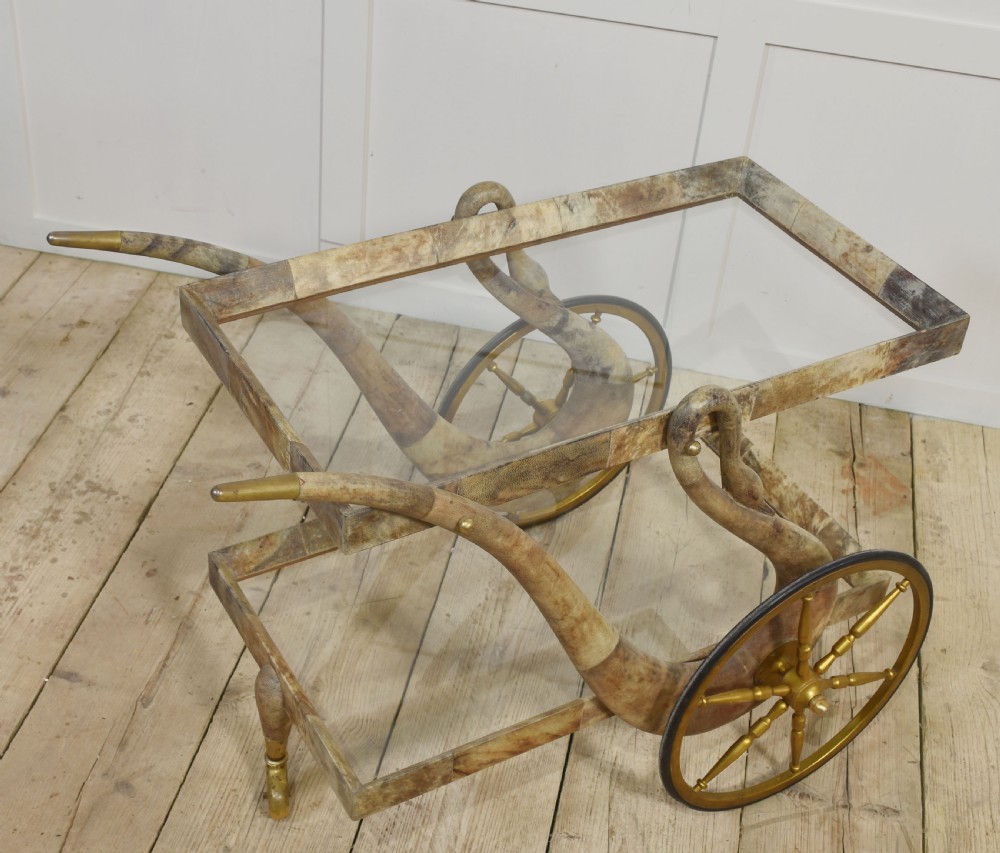 An Italian mid-century drinks trolley crafted with a lacquered goatskin frame, two glass shelves, brass-spoked wheels, and curved handles. View IV