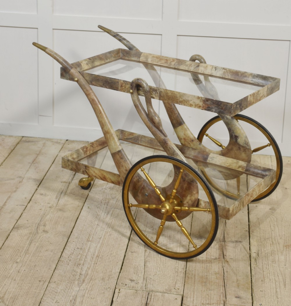 An Italian mid-century drinks trolley crafted with a lacquered goatskin frame, two glass shelves, brass-spoked wheels, and curved handles. View VI