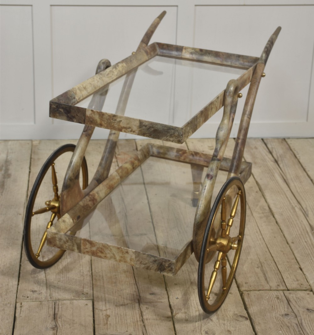 An Italian mid-century drinks trolley crafted with a lacquered goatskin frame, two glass shelves, brass-spoked wheels, and curved handles. View VII