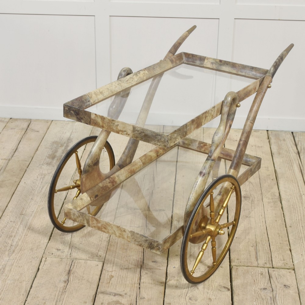An Italian mid-century drinks trolley crafted with a lacquered goatskin frame, two glass shelves, brass-spoked wheels, and curved handles. View IX