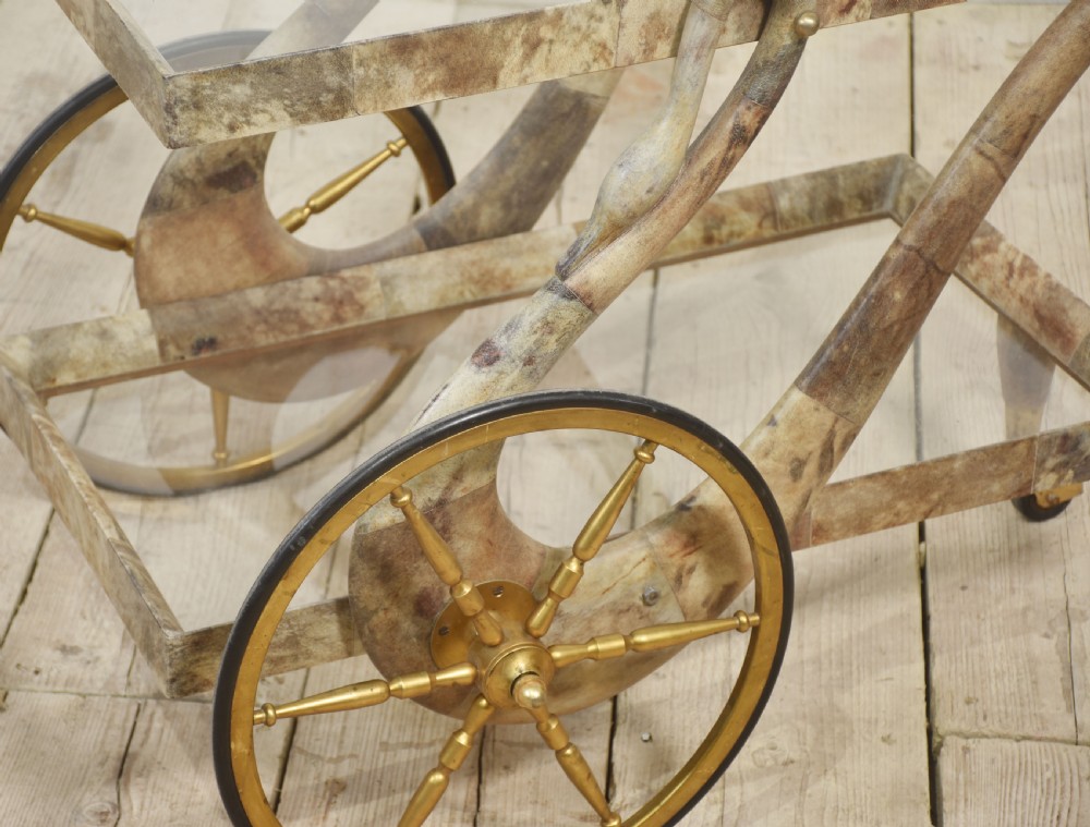 An Italian mid-century drinks trolley crafted with a lacquered goatskin frame, two glass shelves, brass-spoked wheels, and curved handles. View XI