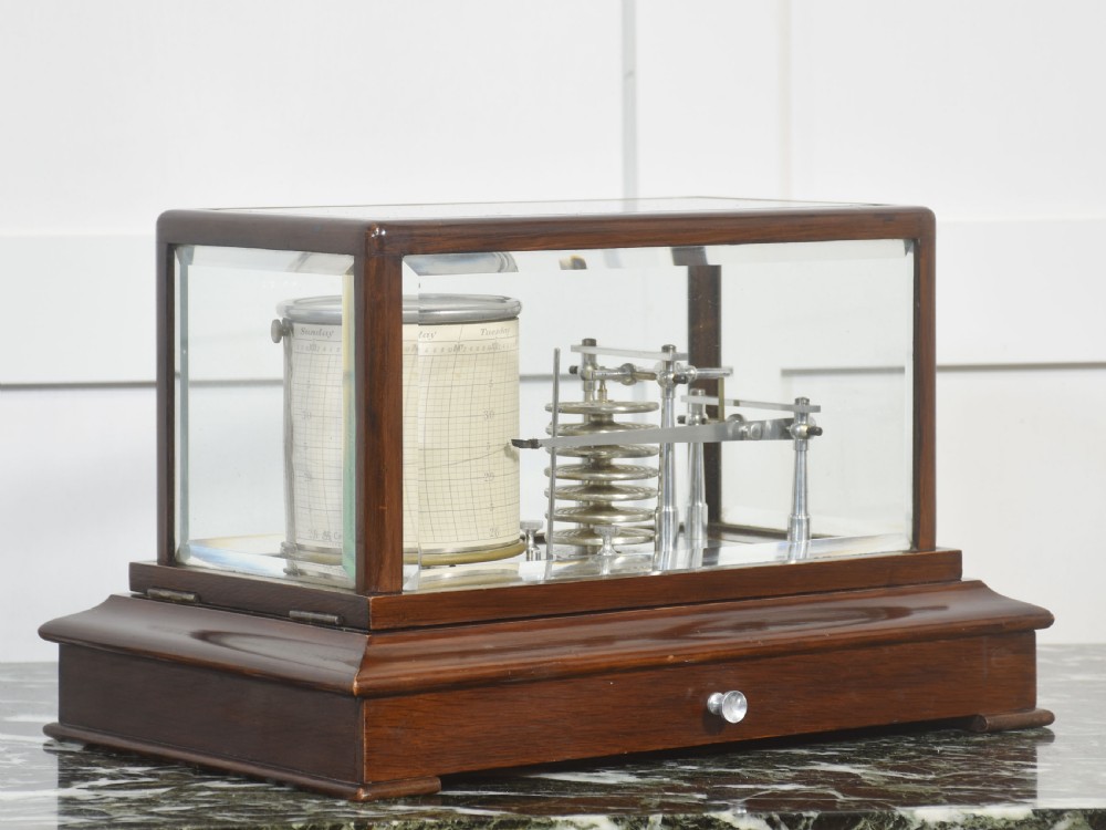 An antique mahogany cased barograph featuring bevelled glass panels enclosing a brass recording mechanism and paper chart drum above a base drawer.