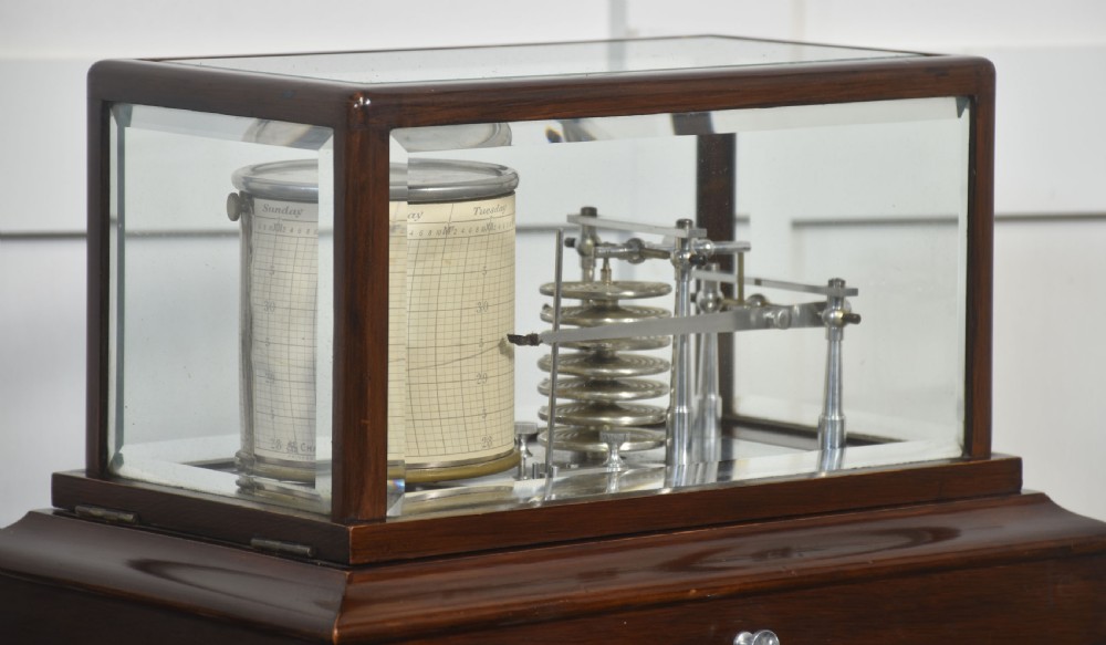 An antique mahogany cased barograph featuring bevelled glass panels enclosing a brass recording mechanism and paper chart drum above a base drawer. View III