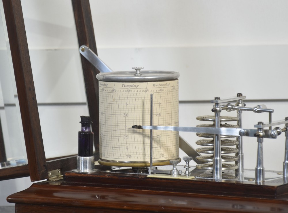 An antique mahogany cased barograph featuring bevelled glass panels enclosing a brass recording mechanism and paper chart drum above a base drawer. View V