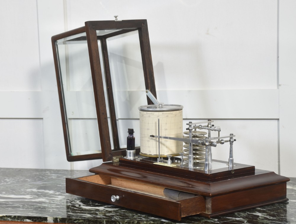 An antique mahogany cased barograph featuring bevelled glass panels enclosing a brass recording mechanism and paper chart drum above a base drawer. View VII