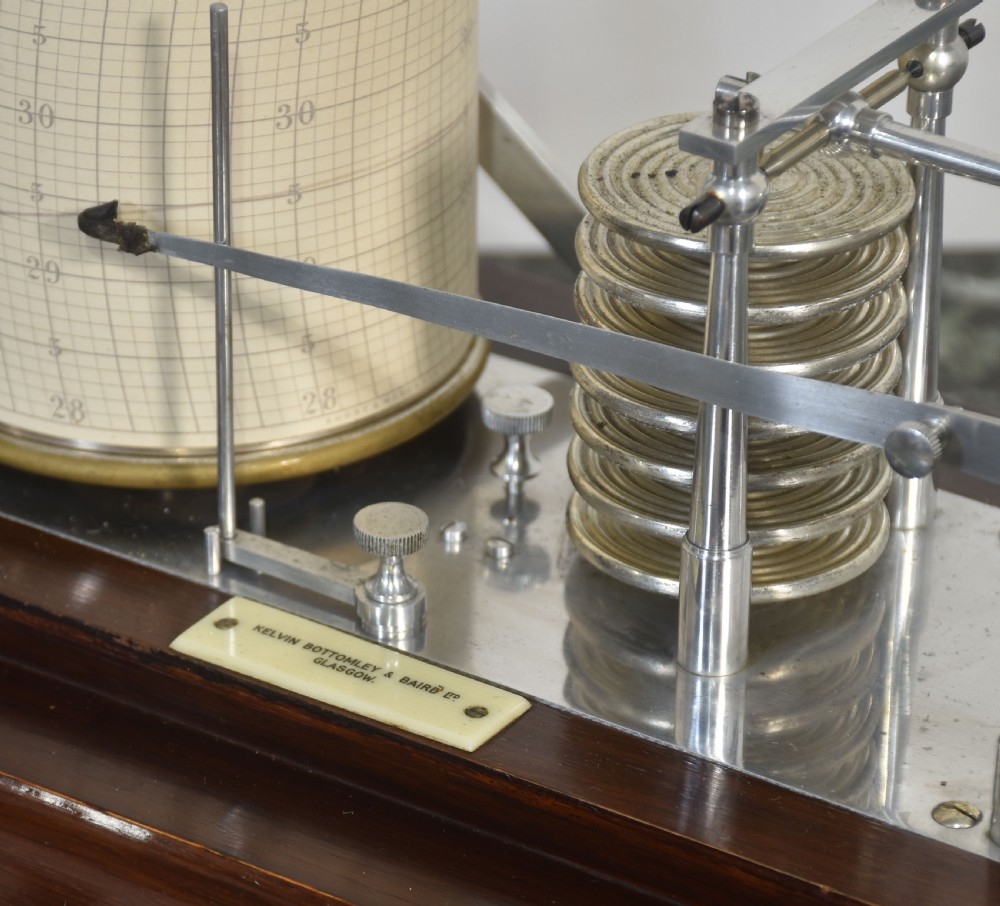 An antique mahogany cased barograph featuring bevelled glass panels enclosing a brass recording mechanism and paper chart drum above a base drawer. View VIII