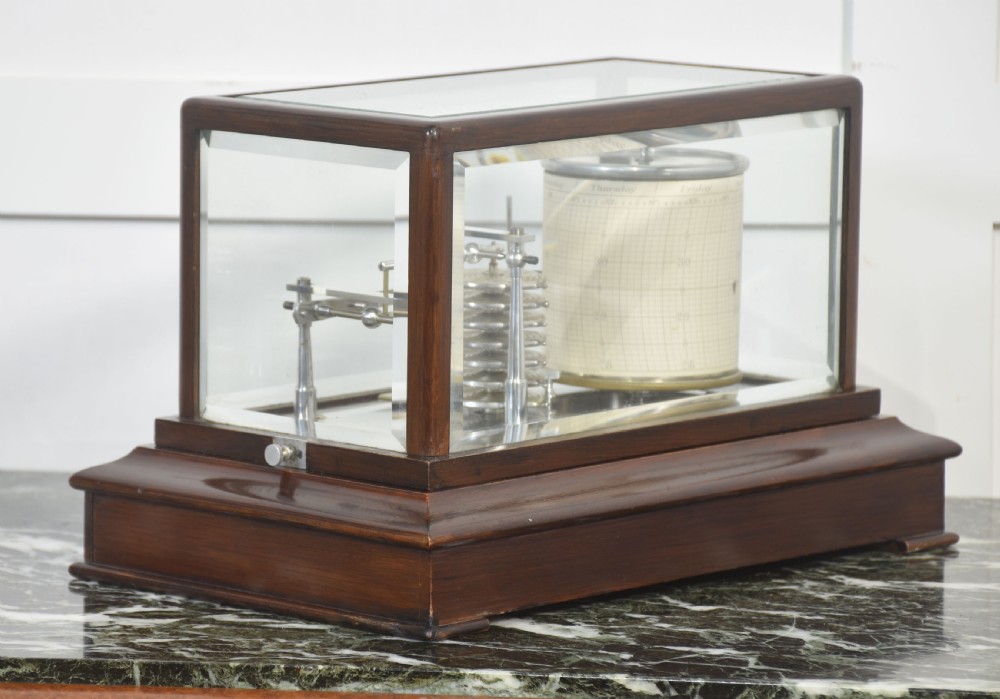 An antique mahogany cased barograph featuring bevelled glass panels enclosing a brass recording mechanism and paper chart drum above a base drawer. View IX