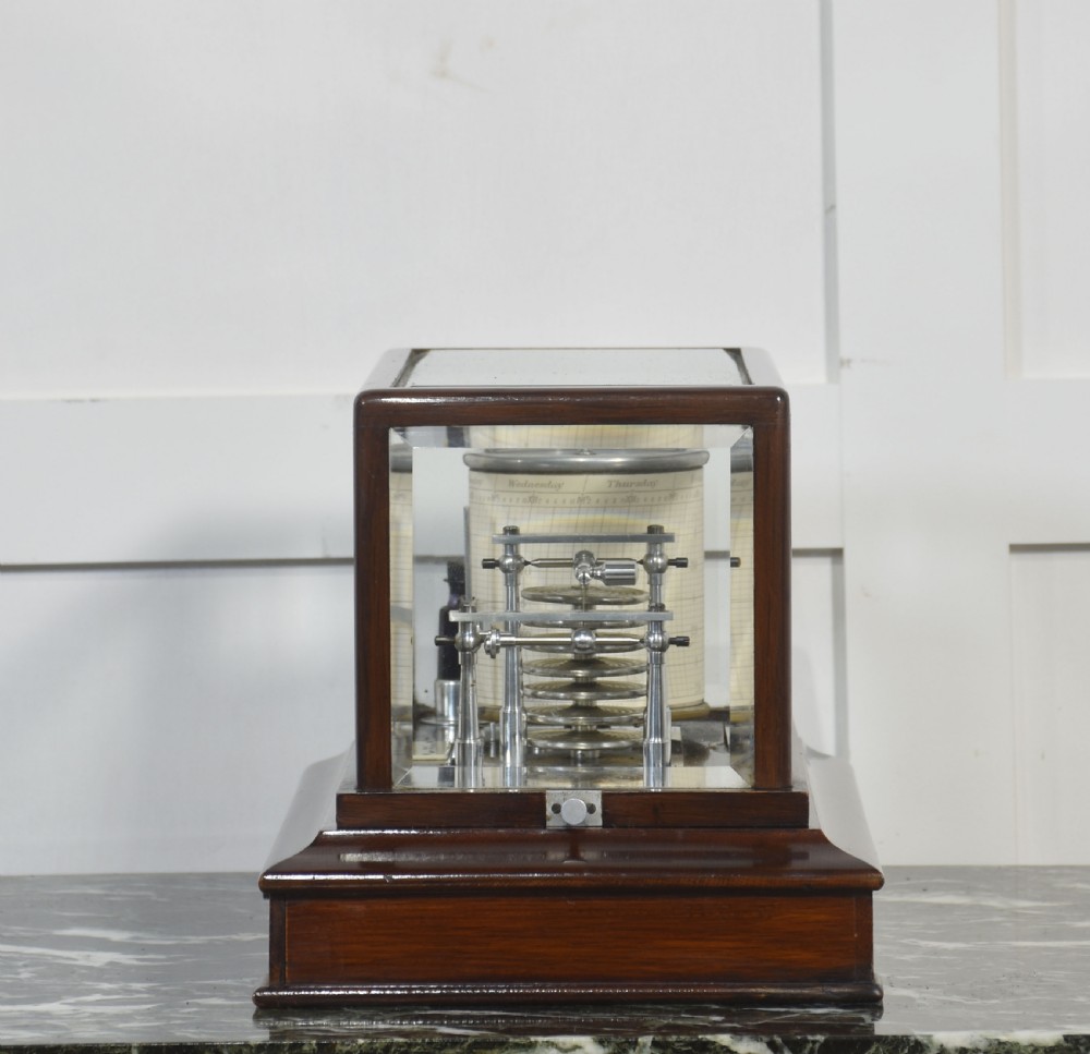 An antique mahogany cased barograph featuring bevelled glass panels enclosing a brass recording mechanism and paper chart drum above a base drawer. View X