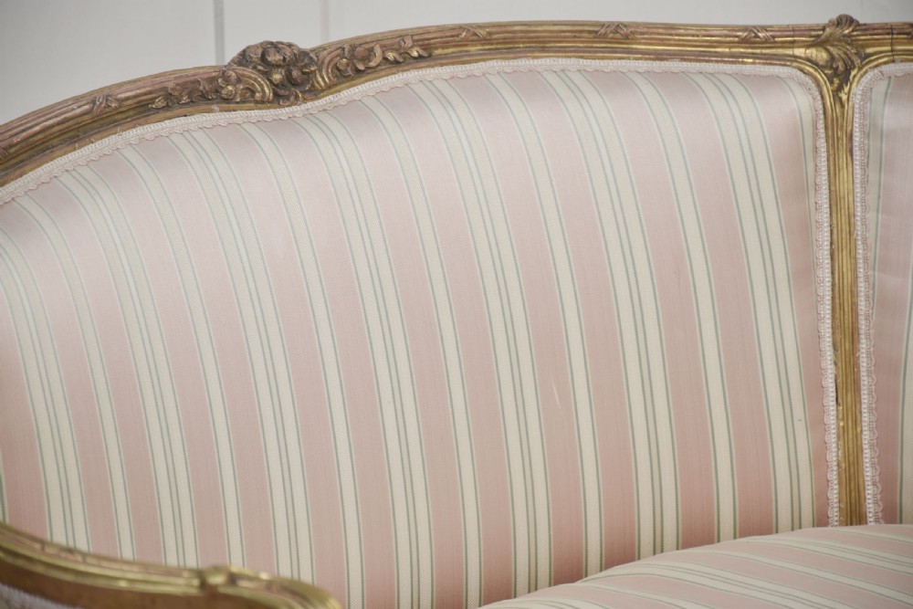 A French Louis XV style giltwood two-seater settee featuring carved floral decorations, curved arms, cabriole legs, and pink and cream striped fabric cushions. View XI