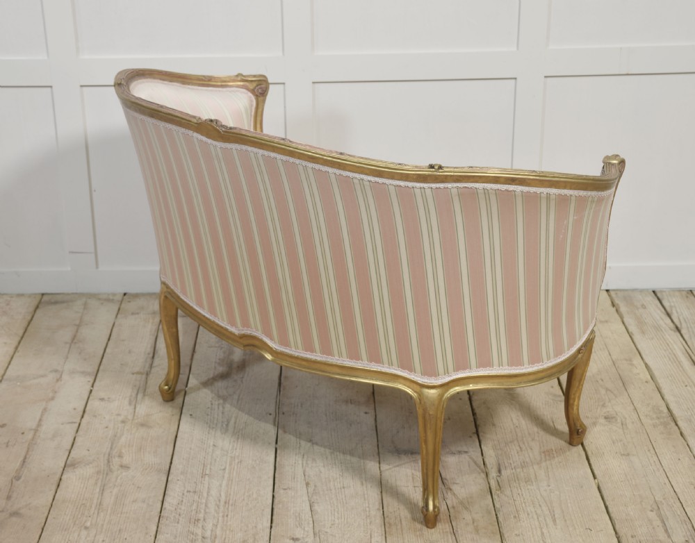 A French Louis XV style giltwood two-seater settee featuring carved floral decorations, curved arms, cabriole legs, and pink and cream striped fabric cushions. View XII