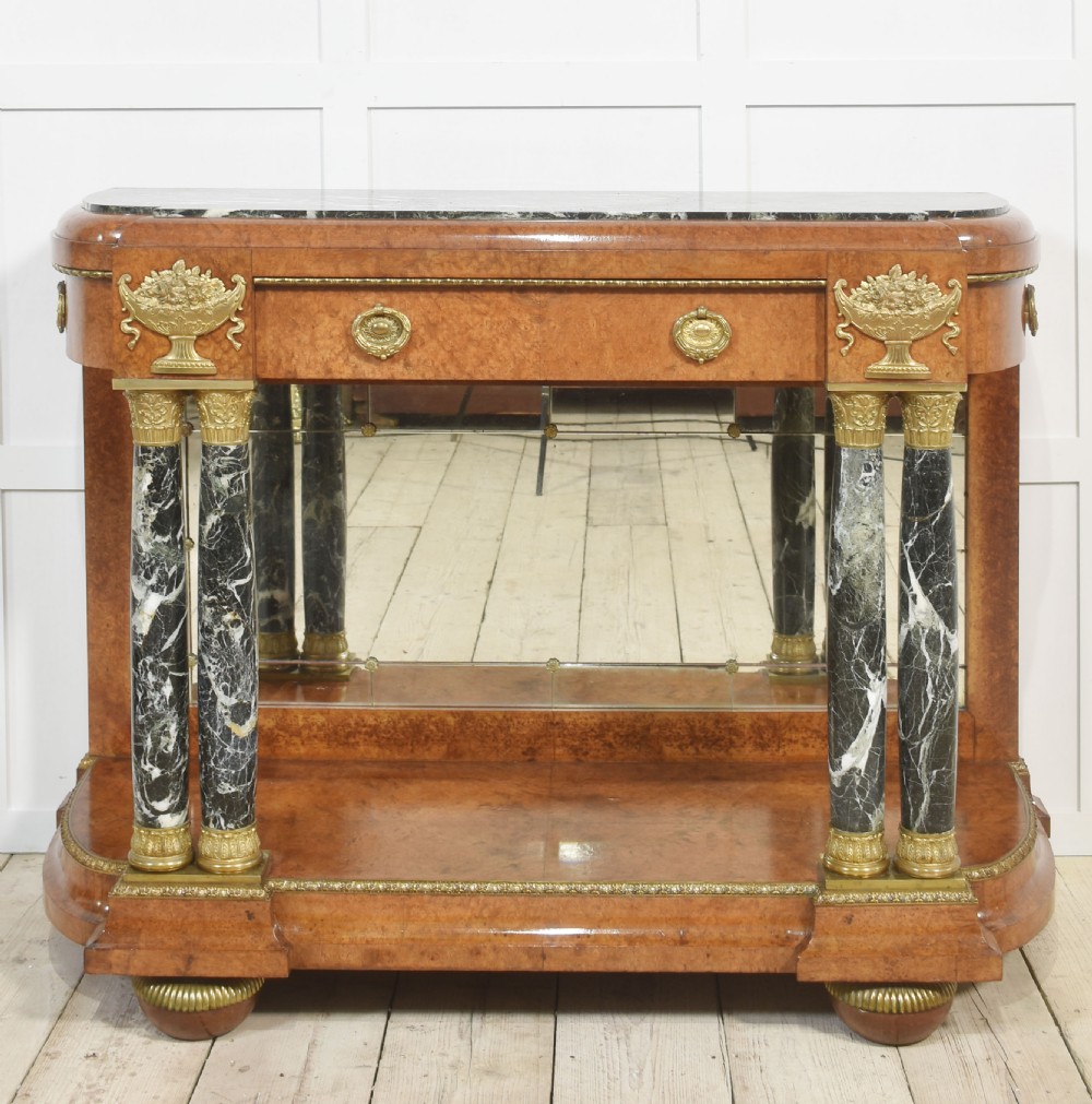 A French style console table with a dark marble top, burr timber veneer, polished marble column supports, gilt bronze mounts, and a mirrored backplate.