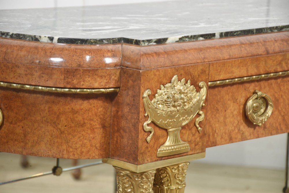A French style console table with a dark marble top, burr timber veneer, polished marble column supports, gilt bronze mounts, and a mirrored backplate. View V