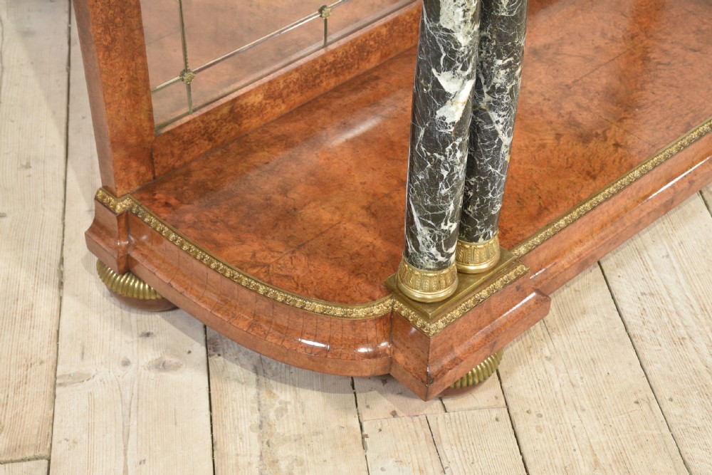 A French style console table with a dark marble top, burr timber veneer, polished marble column supports, gilt bronze mounts, and a mirrored backplate. View VI