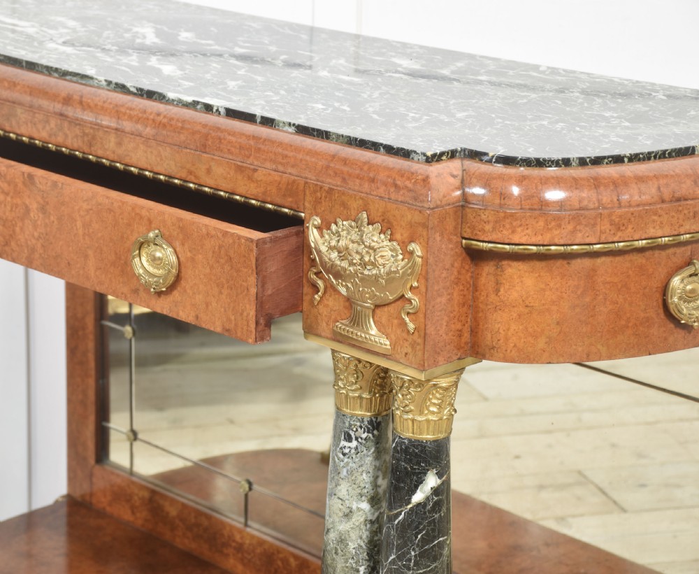 A French style console table with a dark marble top, burr timber veneer, polished marble column supports, gilt bronze mounts, and a mirrored backplate. View IX