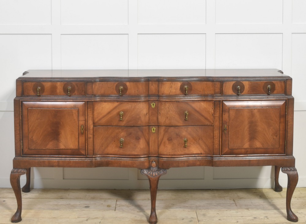 A wide walnut crossbanded Queen Anne style sideboard featuring multiple drawers, cupboard doors, drop brass handles, and carved cabriole legs.