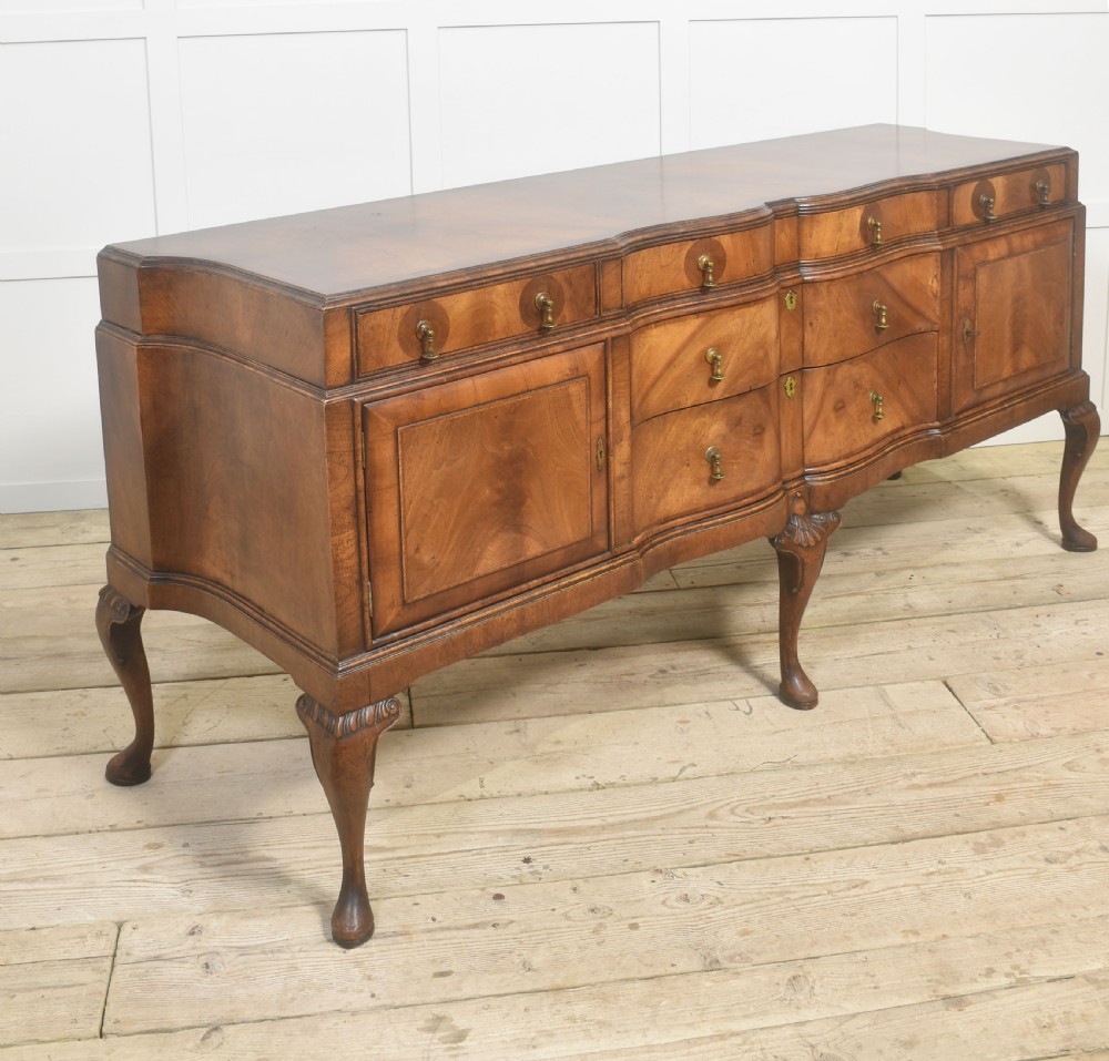 A wide walnut crossbanded Queen Anne style sideboard featuring multiple drawers, cupboard doors, drop brass handles, and carved cabriole legs. View X