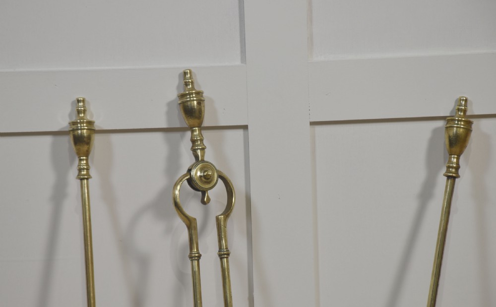 A set of three antique brass fireside tools including a poker, tongs, and a pierced shovel displayed upright. View III