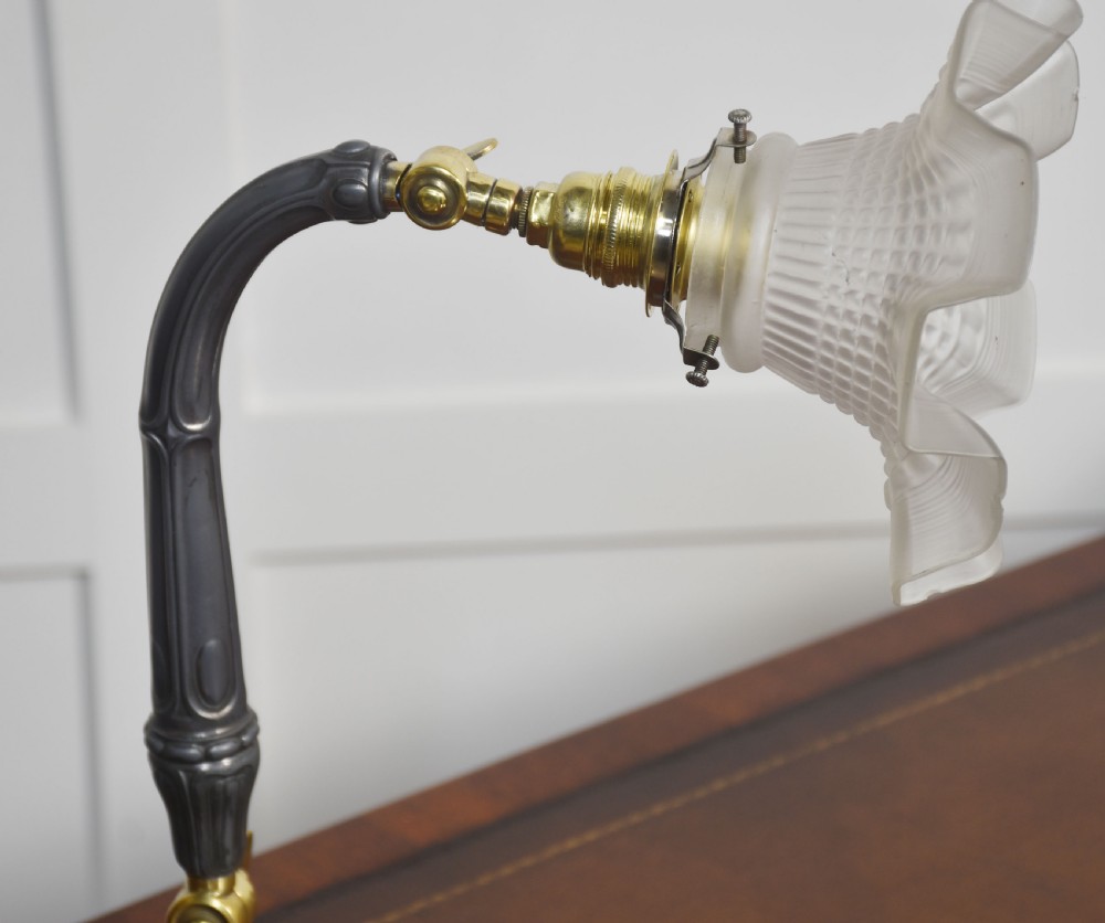 An Art Deco desk lamp with a curved dark grey metal stem, adjustable brass joints, and a frosted glass shade with a flared rim. View X