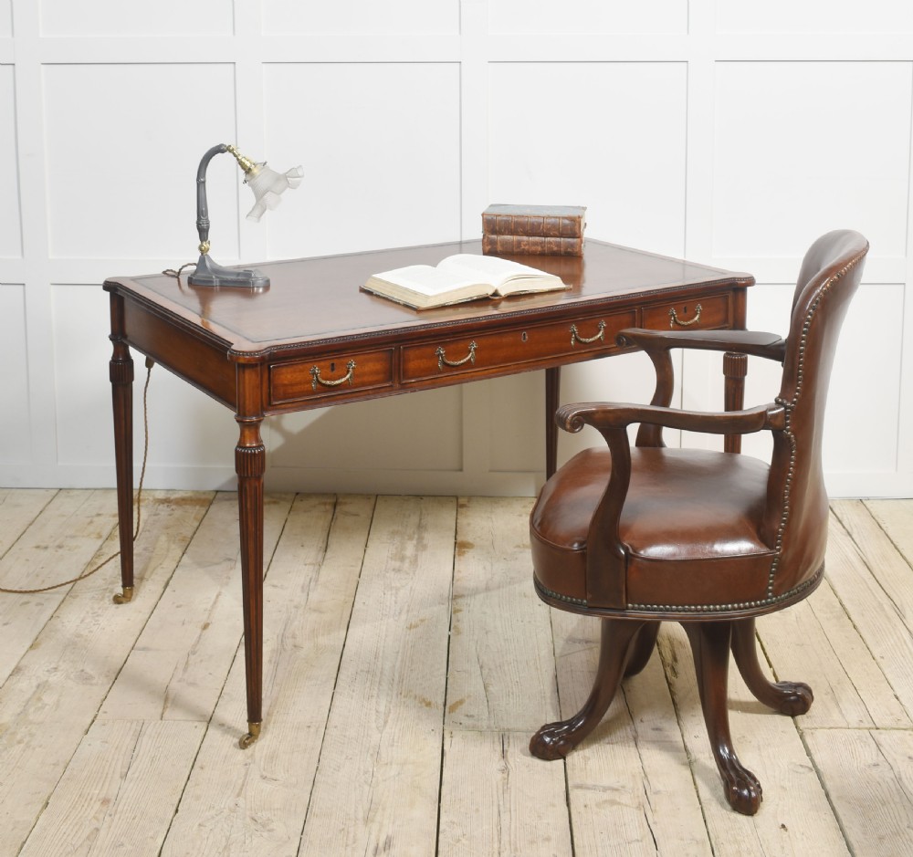 An antique mahogany writing table featuring three frieze drawers with brass handles, a leather inset top, and slim reeded legs with brass castors. View II