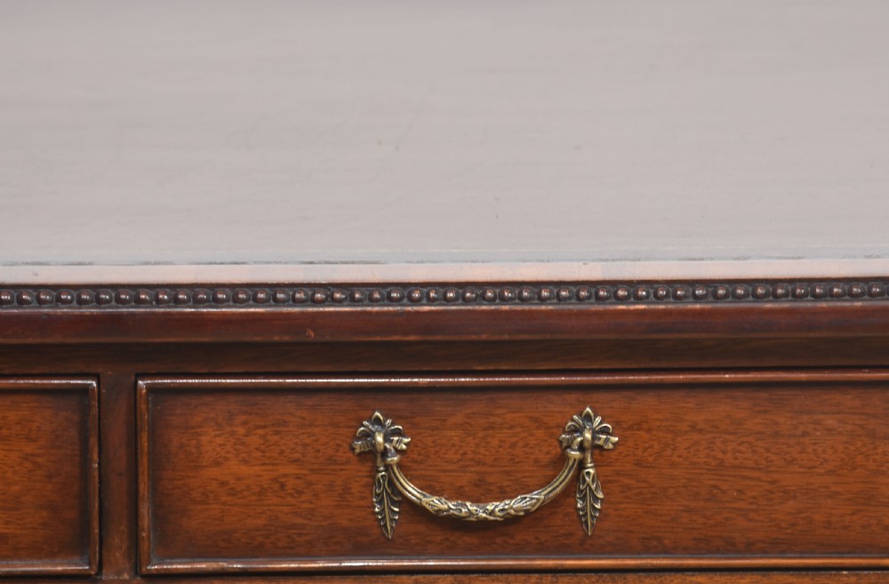 An antique mahogany writing table featuring three frieze drawers with brass handles, a leather inset top, and slim reeded legs with brass castors. View VIII
